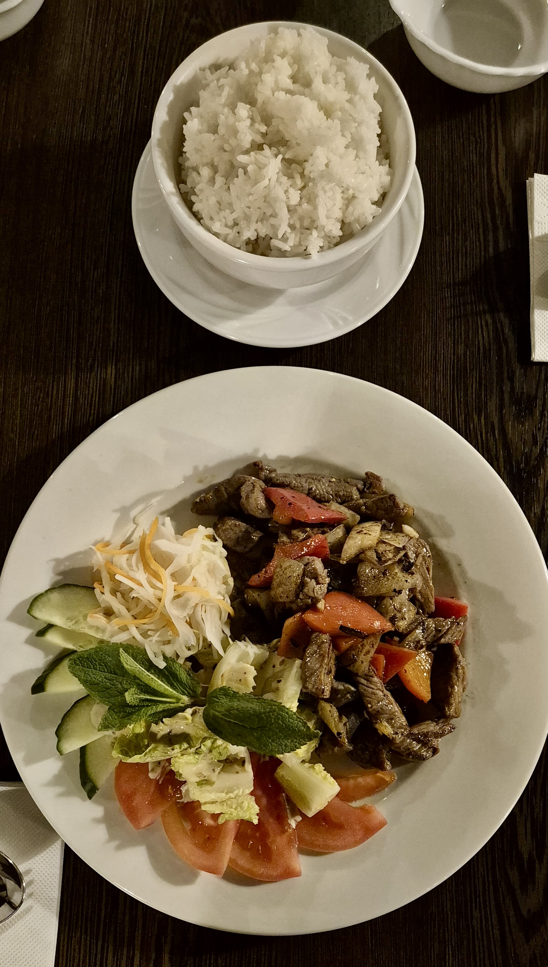 Bò Lúc Lắc – karamellisierte Rindfleischwürfel auf Salatbett mit Zwiebeln, Tomaten und Limette, angerichtet auf schwarzem Steinteller
